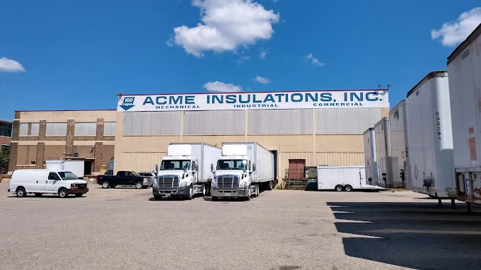 Acme Insulations warehouse exterior with company sign and trucks at the loading dock
